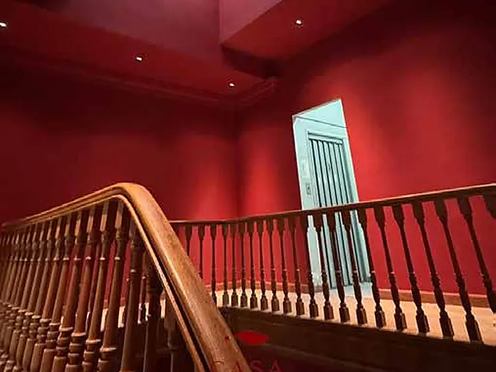 Núcleo de escaleras de Casa VEBE pintado en el bordó de la marca, con la baranda de madera restaurada