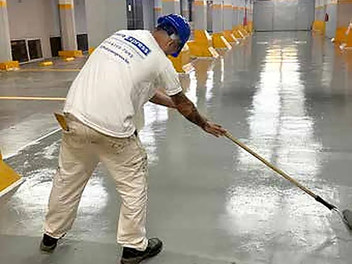 Operario de Pintura Express aplicando pintura epoxi con rodillo de extensión en el estacionamiento del Gobierno de la Ciudad