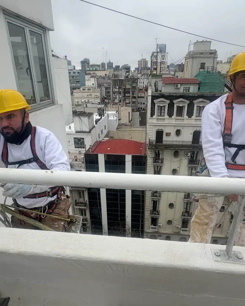 Operario de Pintura Express con casco de seguridad y arnés en la terraza de un edificio, durante un trabajo en altura