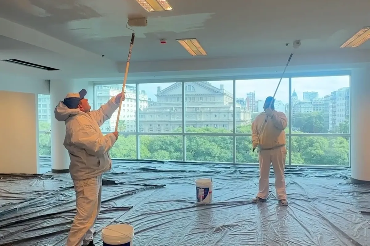 Dos pintores de Pintura Express pintando el cielorraso de una planta de oficinas con rodillos de extensión y el piso totalmente protegido